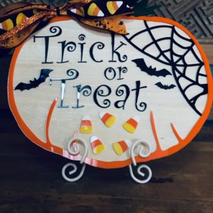 Trick or treat plaque with black spider webs and candy corn.